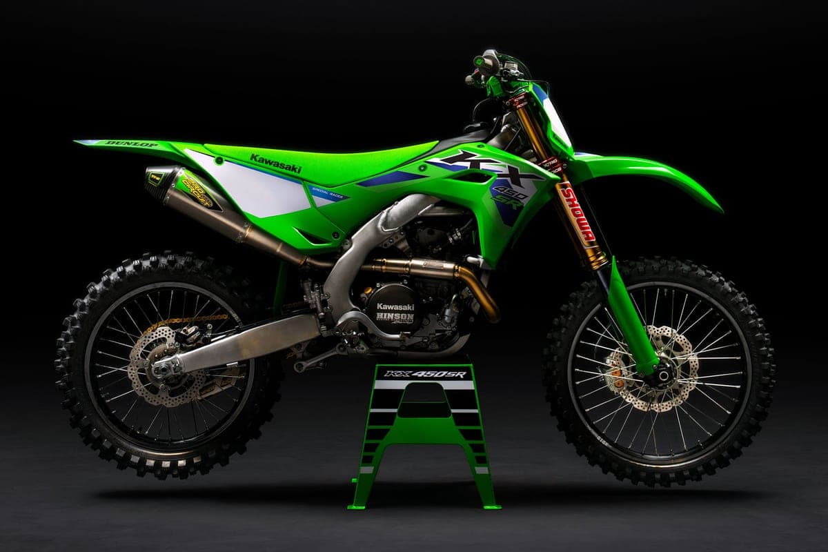 Kawasaki KX450SR shown on a green bike stand against a dark backdrop, side profile highlighting the gold fork legs and works-style pipe