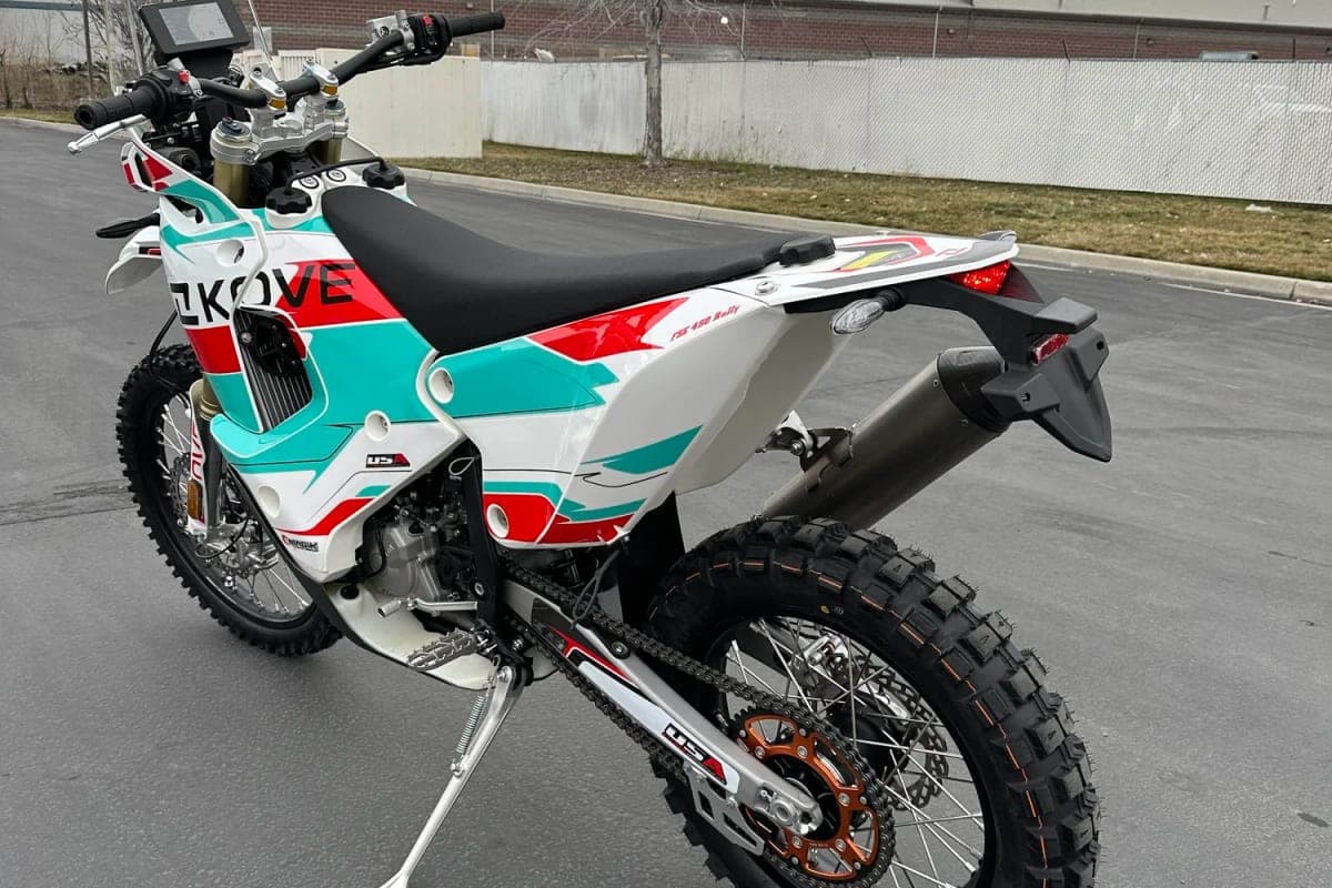 Kove 450 Rally rear three-quarter outdoor shot showing the flat seat, USD fork, orange rear disc rotor and stubby muffler