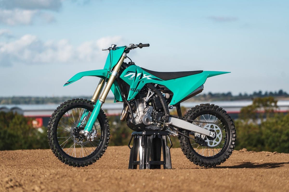 2026 Kove MX450 in bright teal, right-side outdoor studio profile on a motocross track showing the exhaust, chain guard and rear disc brake