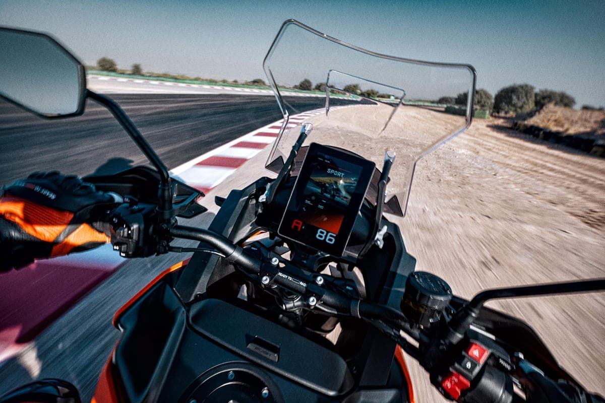 First-person cockpit view riding the KTM 1390 Super Adventure S EVO on a race track, TFT dash reading SPORT with hazard course markers ahead