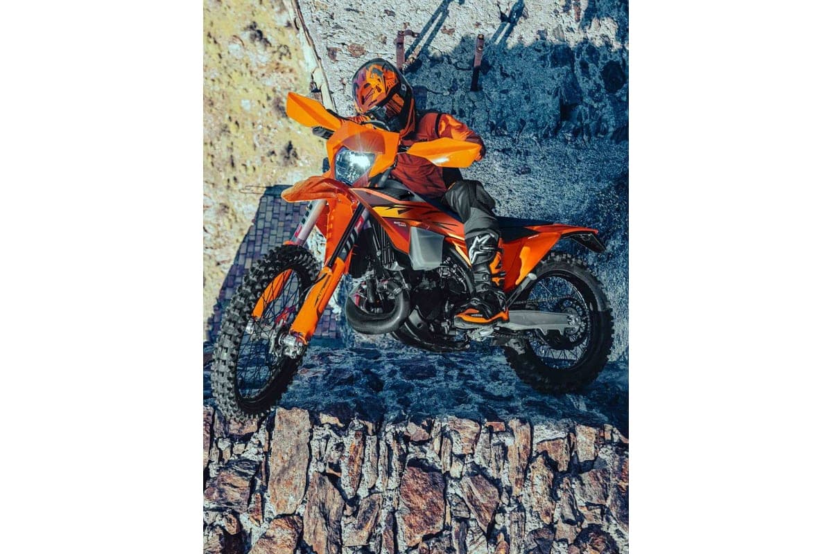 Rider in orange and black gear launching an orange KTM 300 XC-W off a stone ledge, front wheel lofted over rocky terrain
