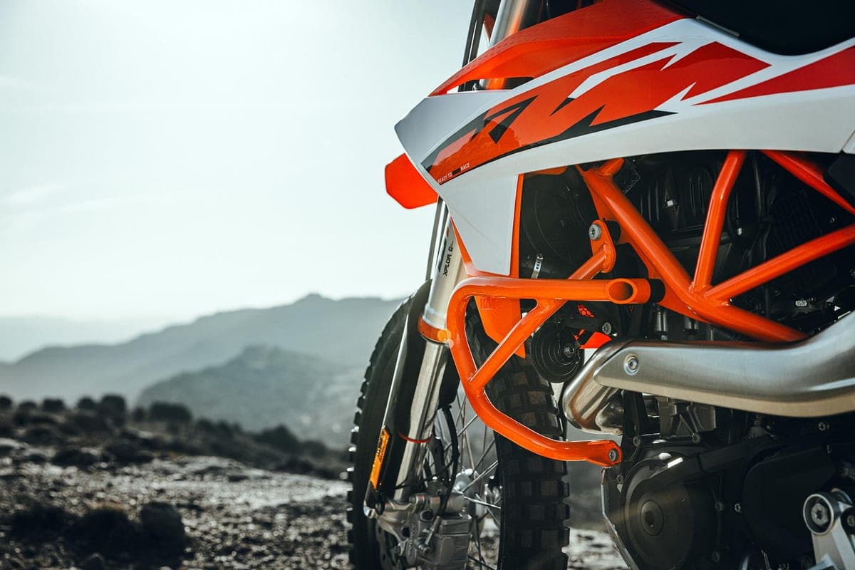 Close-up of the KTM 690 Enduro R's orange trellis frame, chromoly subframe and inverted fork against a hazy mountain backdrop, engine crash bars visible