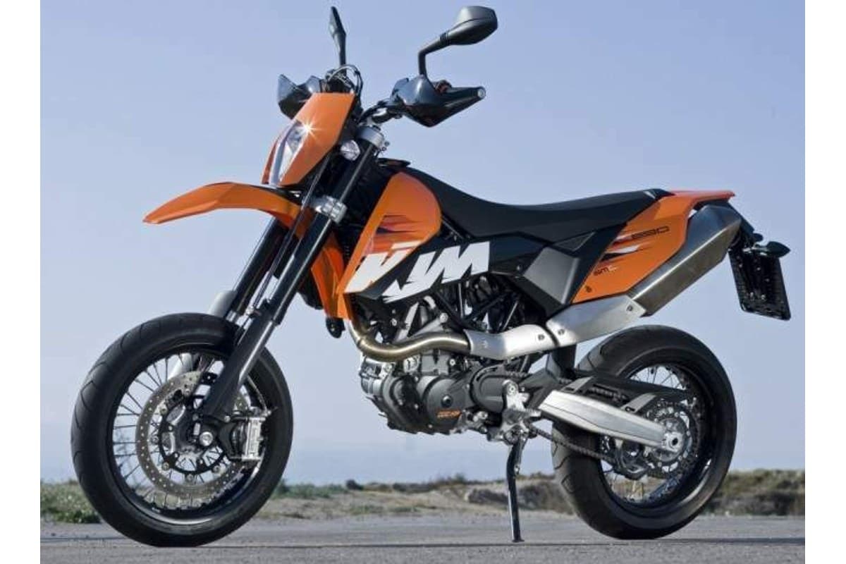 KTM 690 SMC in orange and black, front three-quarter view outdoors against a blue sky, showing the headlight, front disc brake and single-sided-look swingarm
