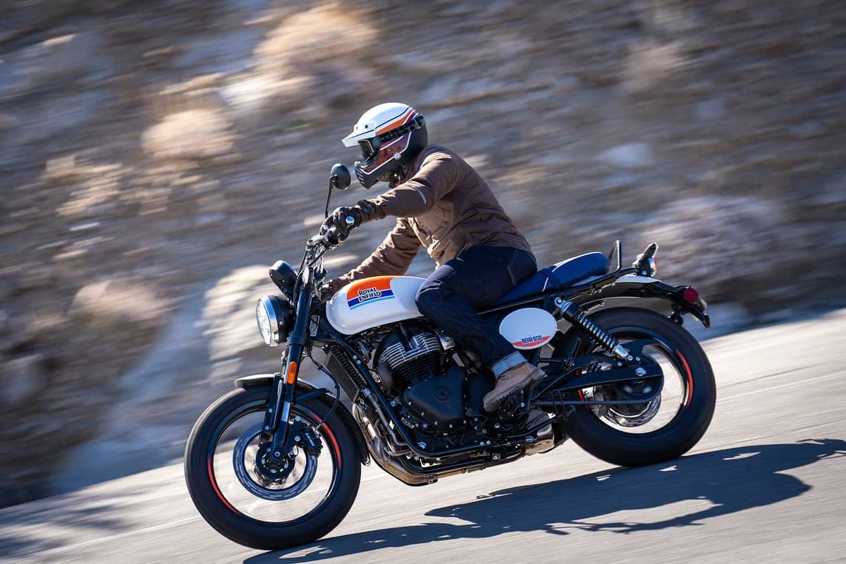 Rider in a white helmet and tan jacket leaning the Bear 650 through a fast road corner in white and blue livery