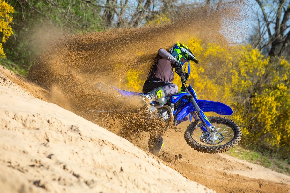 Rider in grey and green gear leaning into a steep sandy bank on a blue Sherco 500 SEF Factory, kicking up a large roost of dirt