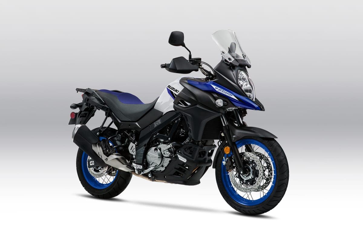 Suzuki V-Strom 650XT in white and blue, front three-quarter studio view on a gradient background highlighting the beak fender, twin headlights and long-travel forks