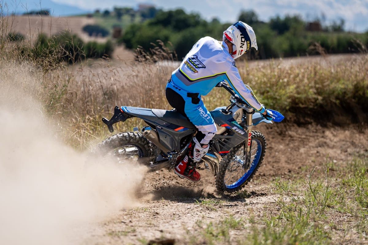 Rider in white and blue Circuit gear powering the gray TM EN 250 FI 2T through a dusty dirt corner, kicking up a large roost of sand