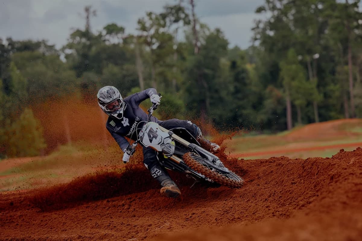 Rider in white and black gear cornering the Triumph TF 450-RC through a red-clay motocross berm