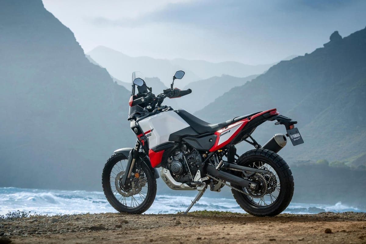 Yamaha Ténéré 700 World Raid parked rear three-quarter on a coastal dirt overlook with rocky cliffs and ocean waves behind it