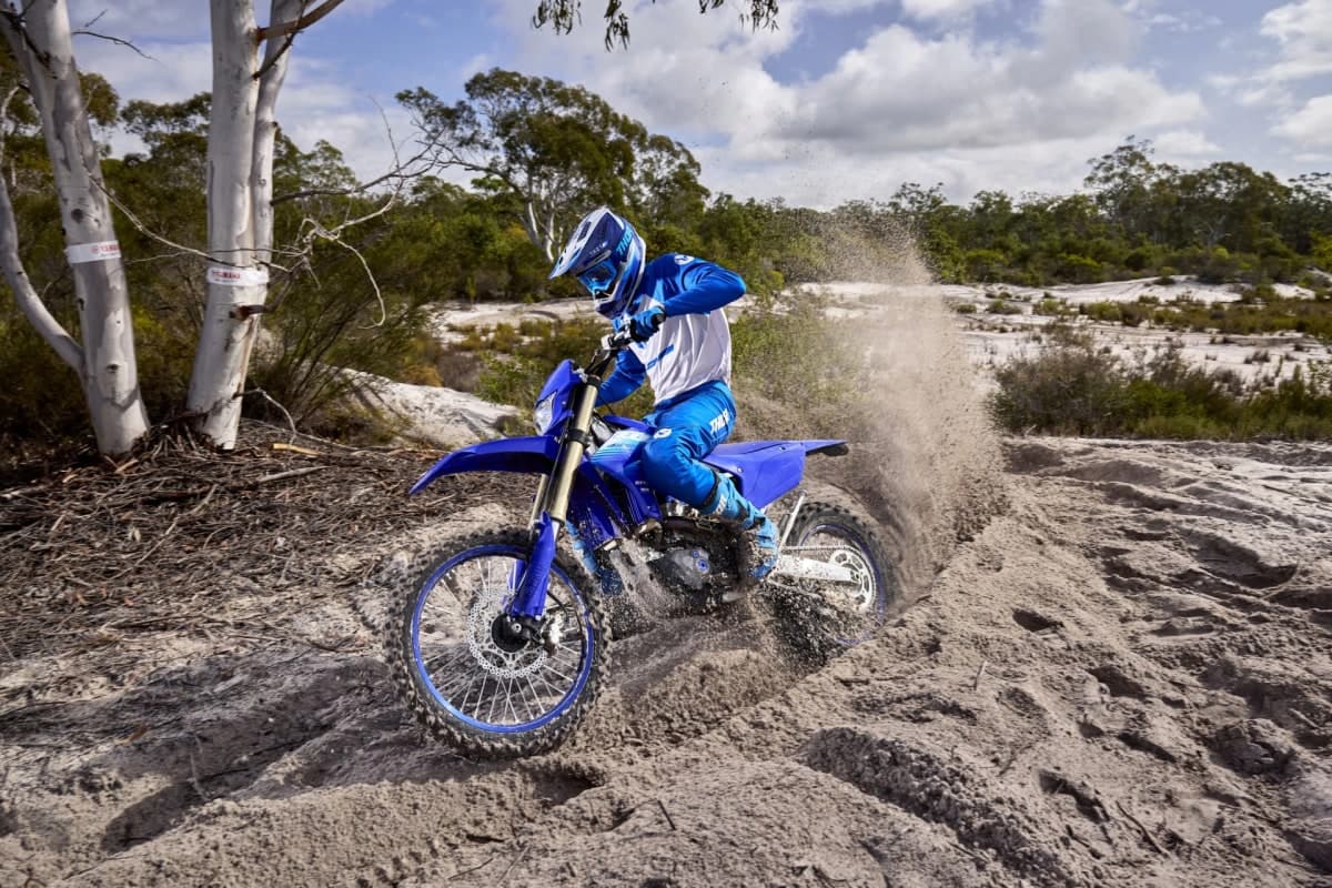 Rider in blue gear roosting the 2027 WR450F through a sandy turn, throwing a plume of sand from the rear wheel