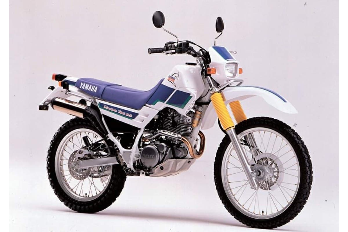 Yamaha XT225 in white with purple seat and gold-anodized forks, left-side studio view highlighting the upswept exhaust and knobby dual-sport tires