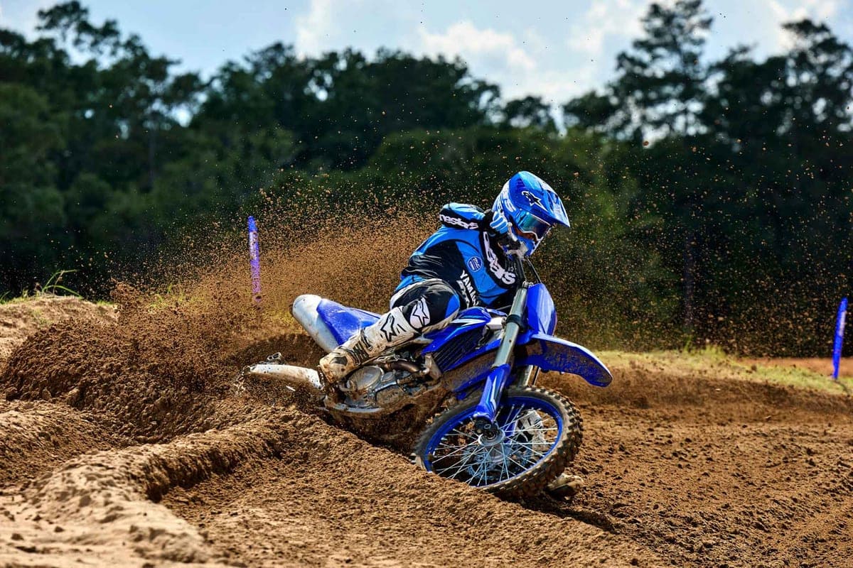 Rider in blue Yamaha gear leaning the YZ250F through a sandy motocross berm, roosting dirt off the rear knobby tire