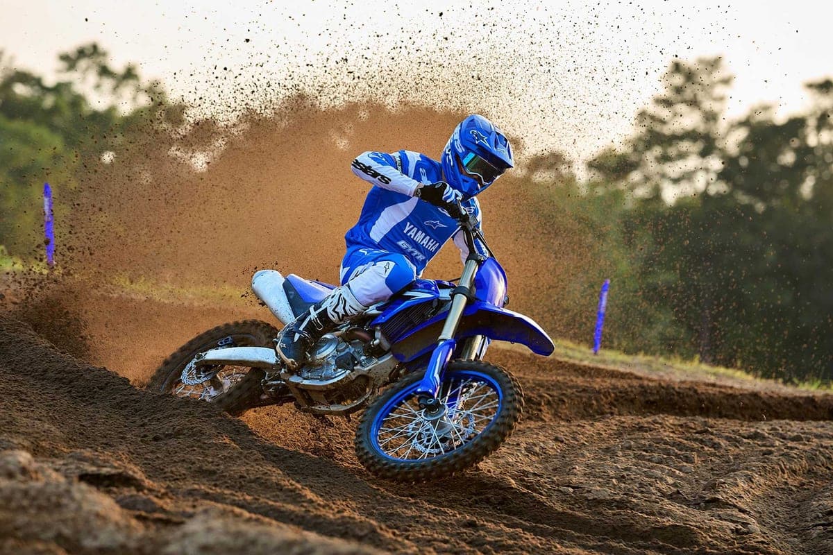 Rider in blue and white Alpinestars gear leaning a Yamaha YZ450F through a dirt berm, kicking up a huge roost of sand