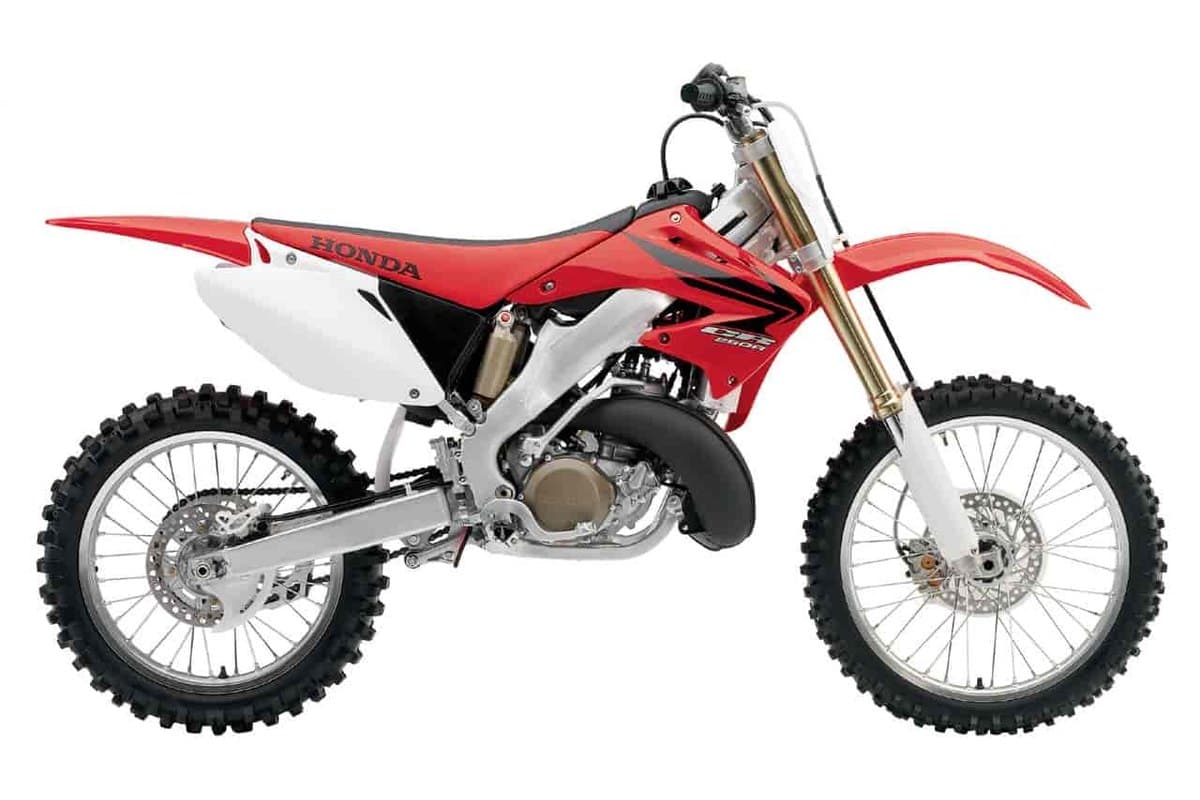 2007 Honda CR250R two-stroke motocross bike in red and white, right-side studio profile showing gold forks and exposed expansion chamber