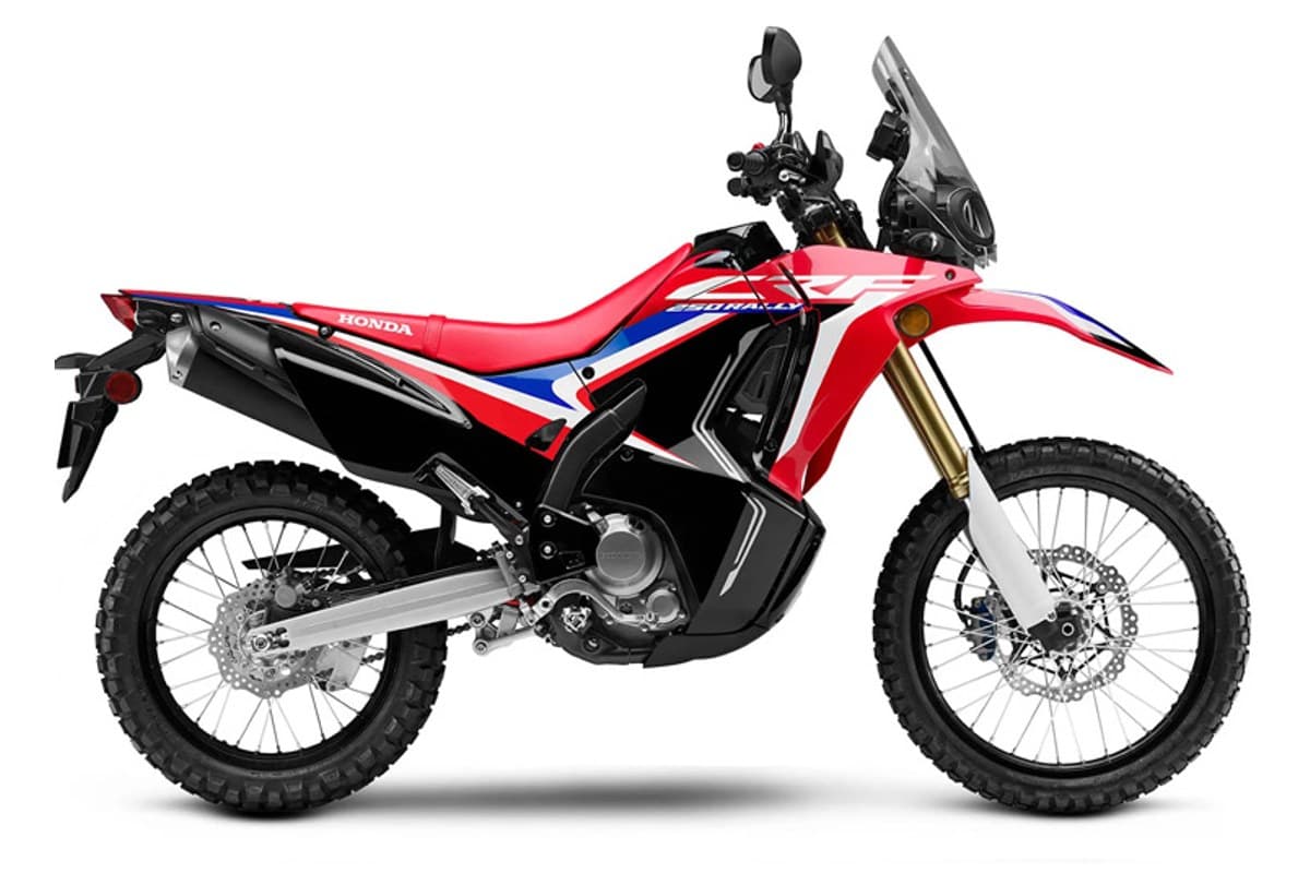 2020 Honda CRF250L Rally in red, white and blue Dakar-style livery, right-side studio profile showing gold forks, tall screen and knobby tires