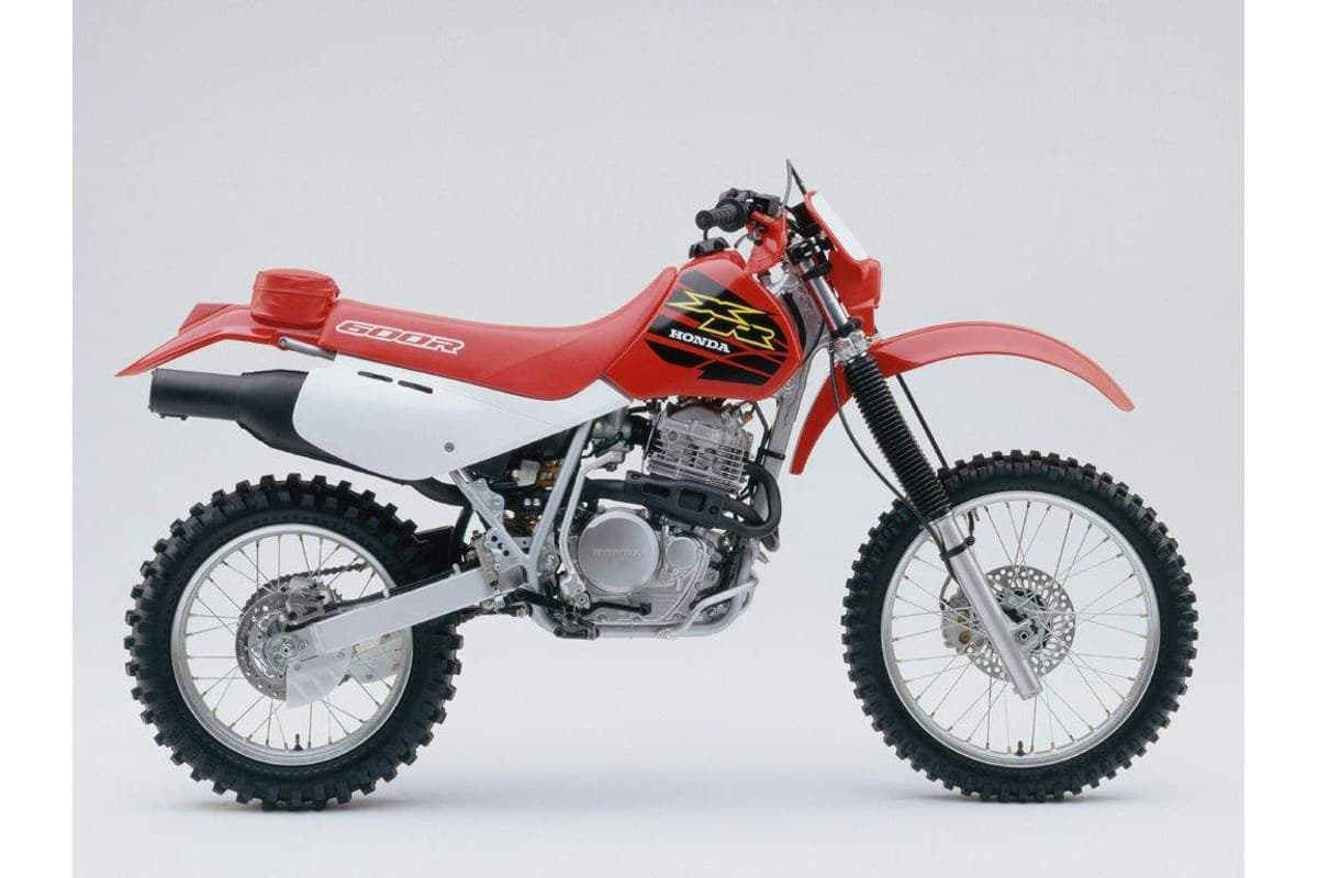 2000 Honda XR600R dual-sport enduro in red and white, right-side studio profile showing the tall front fender, spoked wheels and side-mounted exhaust
