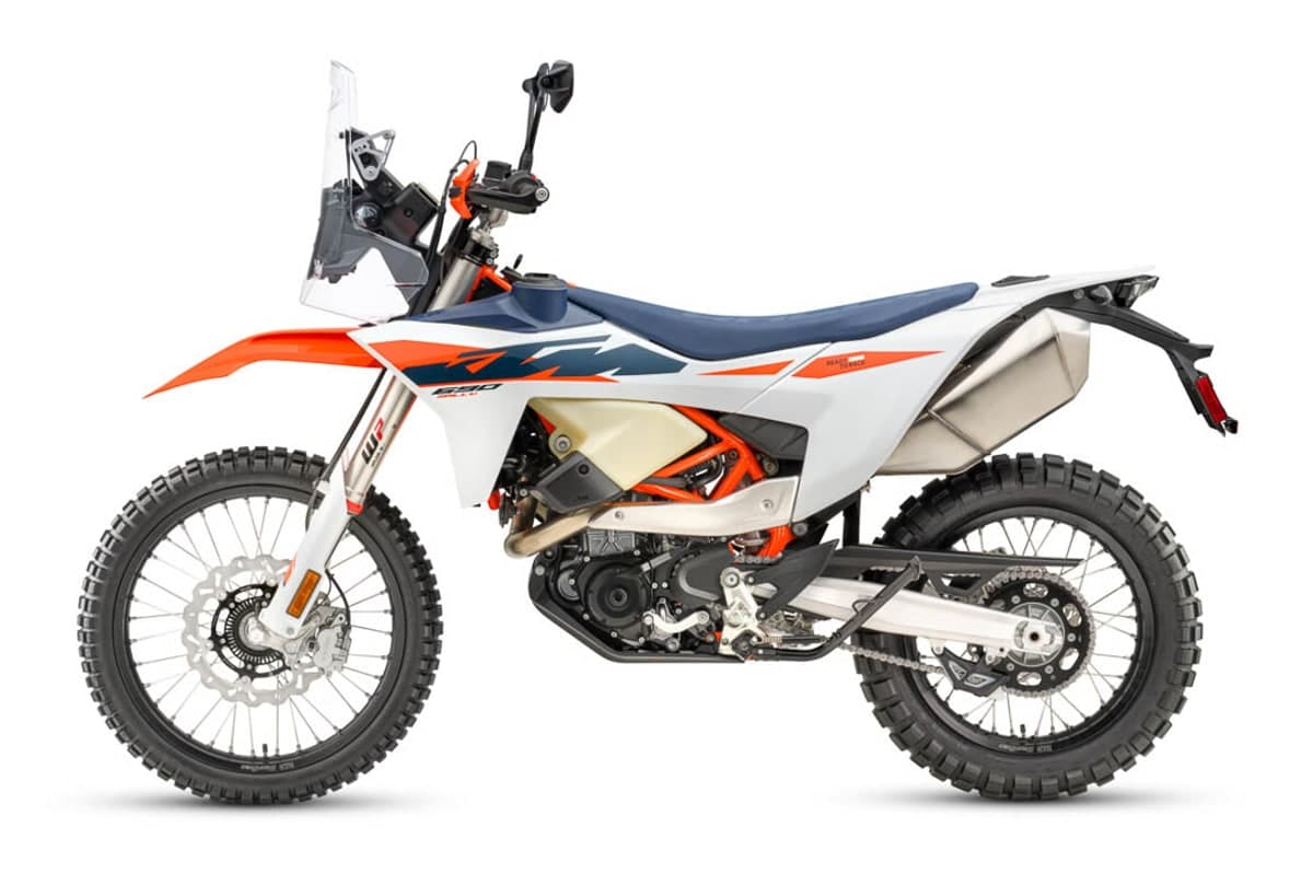 2027 KTM 690 Rally in white, blue and orange, left-side studio profile showing the rally tower, front auxiliary tanks and 21-inch spoked front wheel