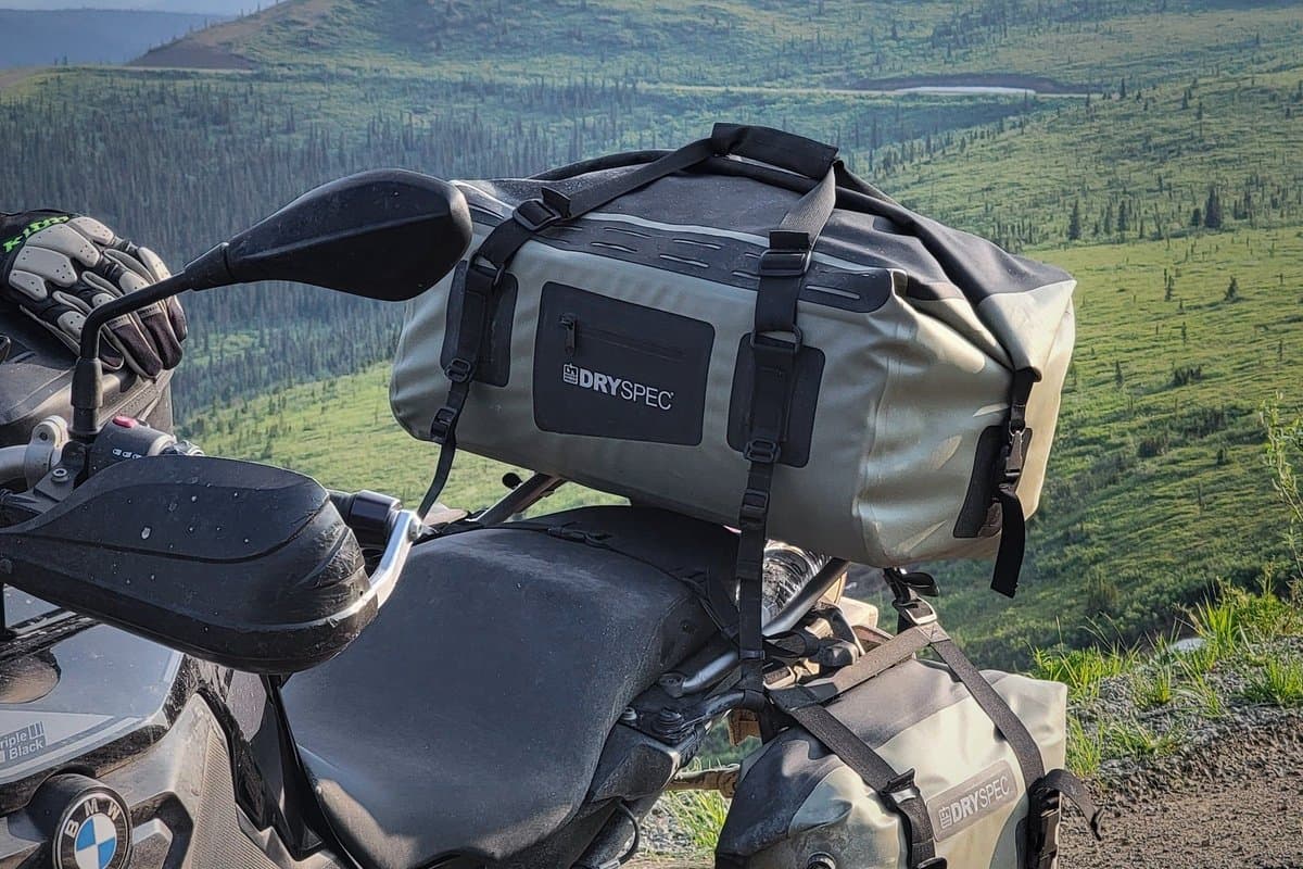 D38 strapped to the seat of a BMW adventure bike on a mountain road