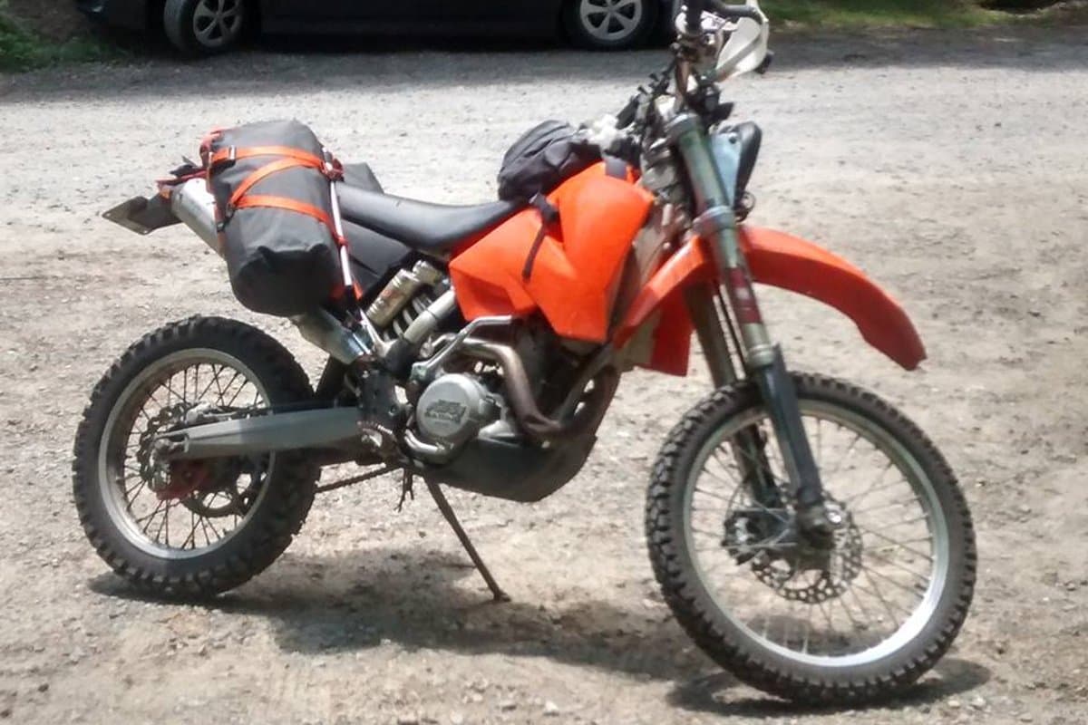 KTM dirt bike with a black roll-top dry bag strapped to the side of the tail on orange straps