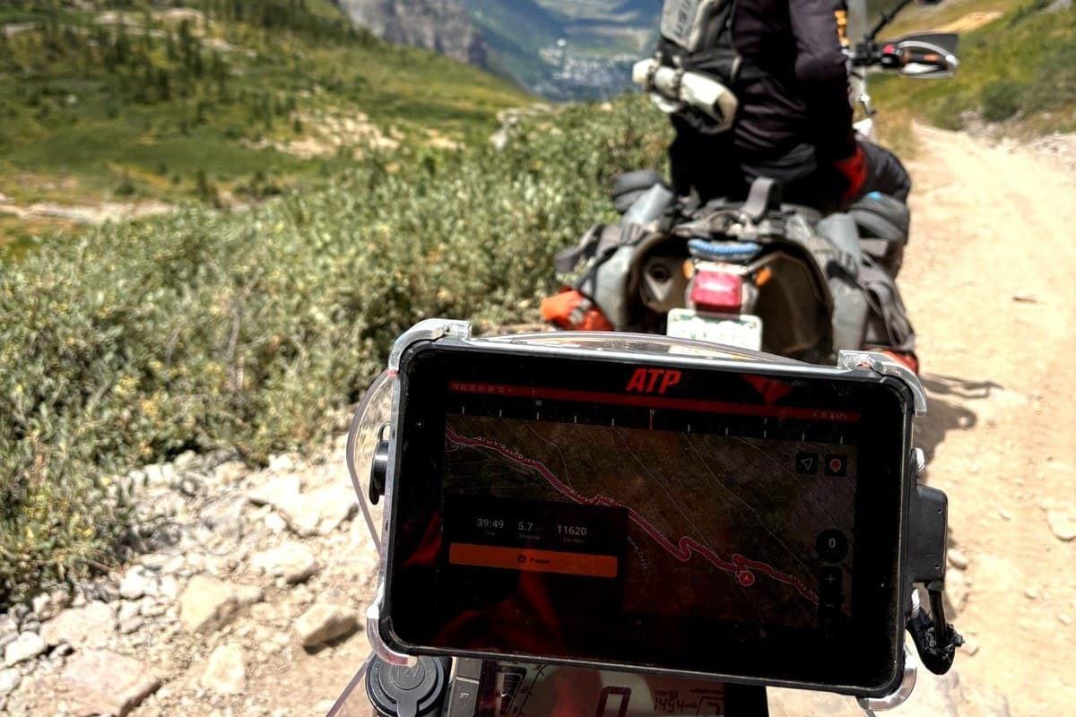 The tablet mounted on an adventure bike's dash, showing a track on a mountain trail behind another rider