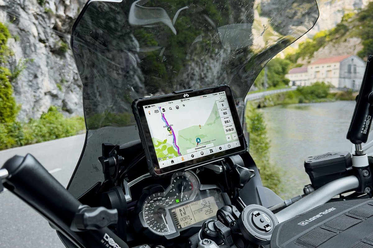 The tablet mounted above the dash of a BMW GS, showing a map, on a road beside a river