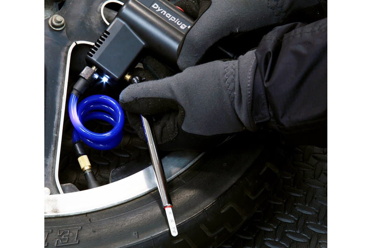 Gloved hand checking pressure with the pencil gauge while the Micro Pro Inflator runs on a tire