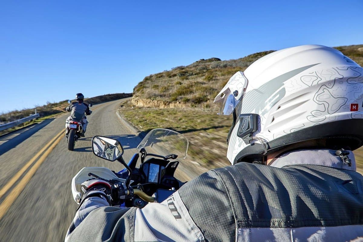 Rider on an adventure bike wearing a white dual sport helmet fitted with the BT Mini, following another rider