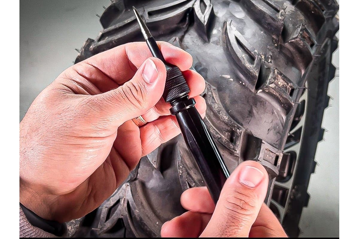 Hands pushing the plug inserter into a puncture on a knobby tire