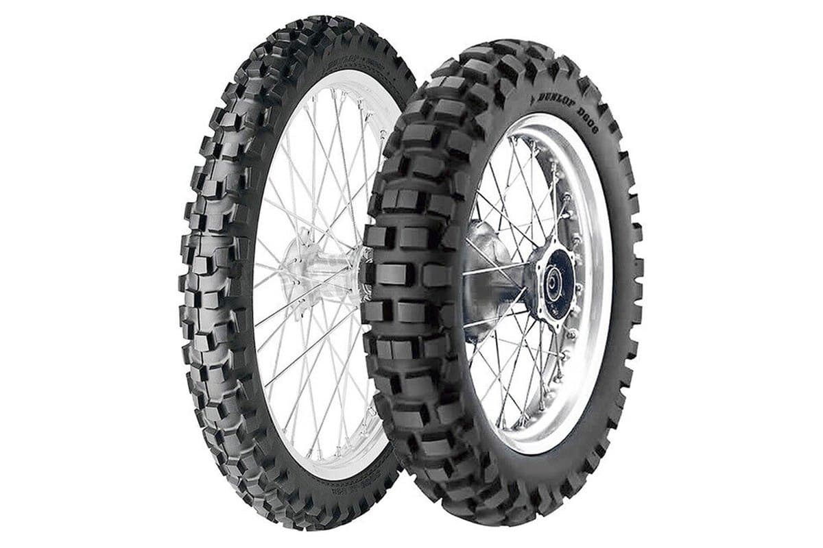 Dunlop D606: front and rear pair mounted on silver spoked wheels, the narrow front at left and the wider knobby rear at right, DUNLOP D606 moulded into the rear sidewall, on white