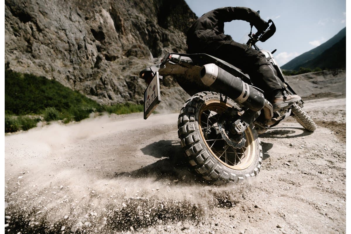Continental TKC 80 Second Generation: a low rear three-quarter of an adventure bike sliding in a gravel pit, the rear tire spraying dust with the knobs in sharp focus