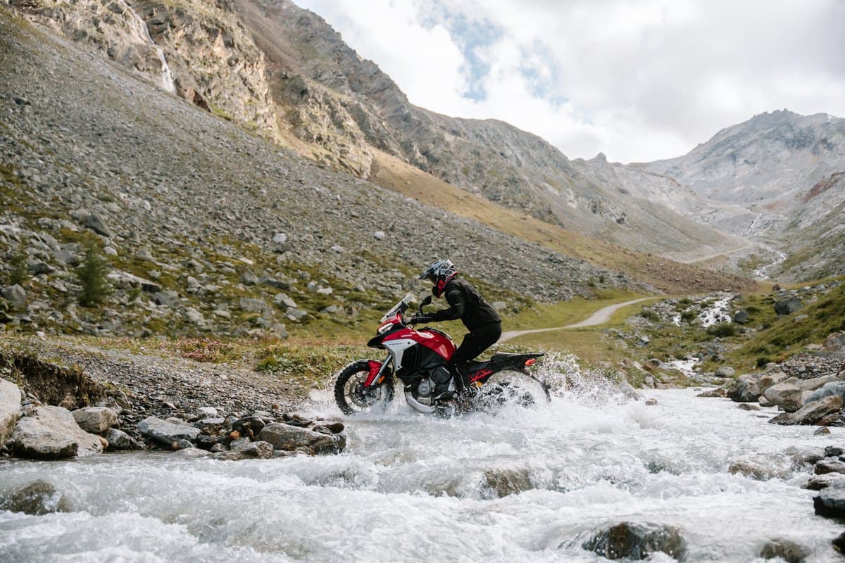 Continental TKC 80 Second Generation: an adventure bike crossing a rocky alpine stream side on, both knobby tires in the water