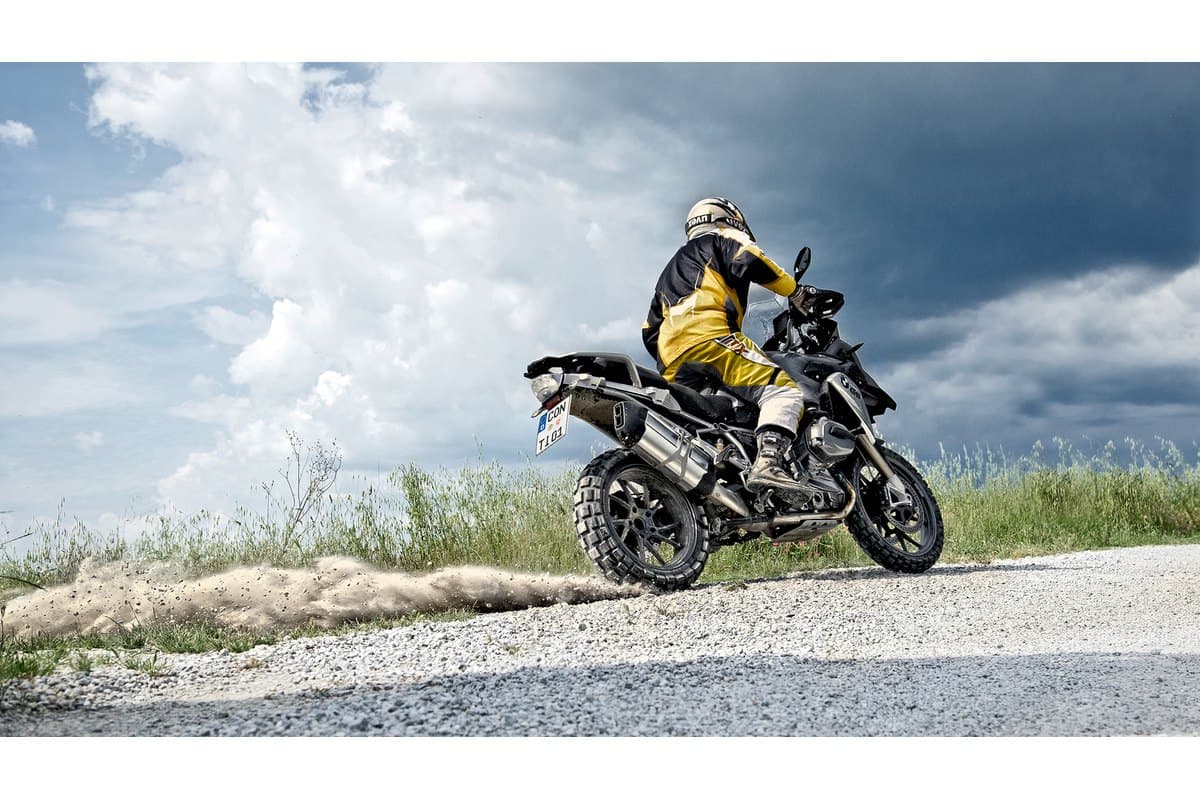 Continental TKC 80 Twinduro: a rider powering off a gravel shoulder with the rear wheel throwing stones, the knobs visible on both wheels