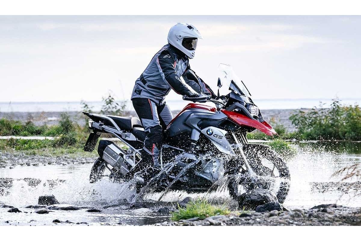 Metzeler Karoo Street: a rider blasting through a shallow water crossing, side view with spray off the wheels