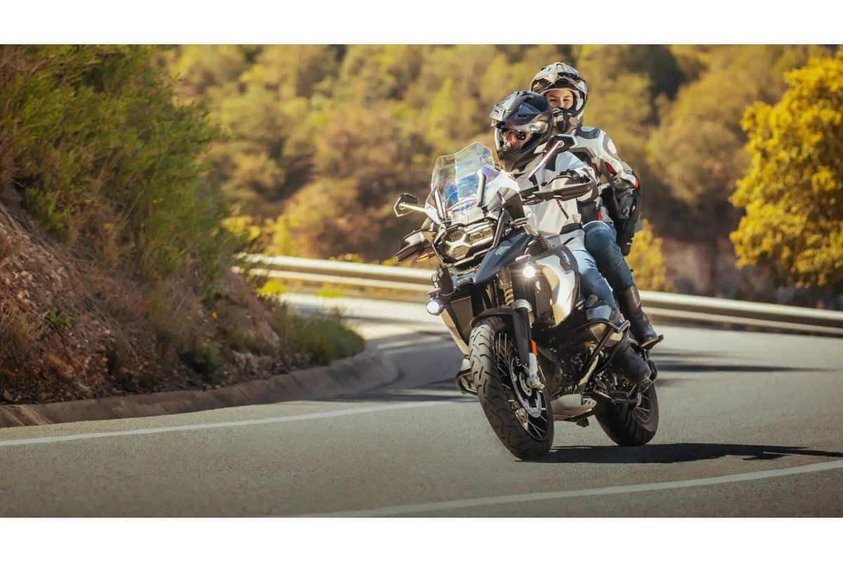 Michelin Anakee Road: two-up riders leaning through a sunlit paved mountain corner, the front tire clearly in frame