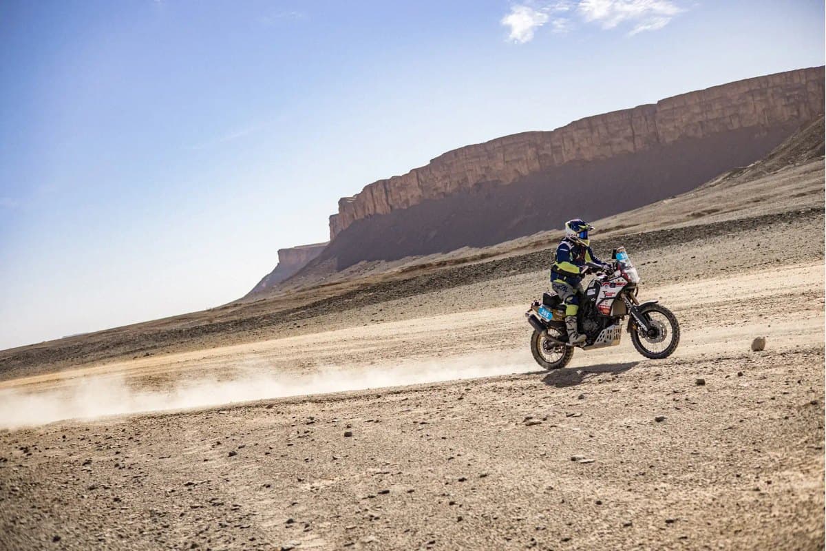 Michelin Desert Race: a rally bike with a navigation tower running flat out across a stony desert plain below a mesa