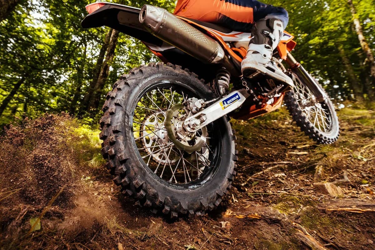 Michelin Enduro Medium 2: low shot of an enduro bike's rear wheel spitting dirt on a forest trail, ENDURO MEDIUM readable on the sidewall