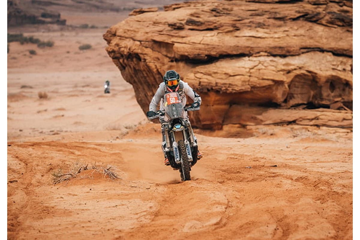 Mitas Enduro Trail-Rally: a rally rider riding toward the camera across red desert sand, a sandstone outcrop behind
