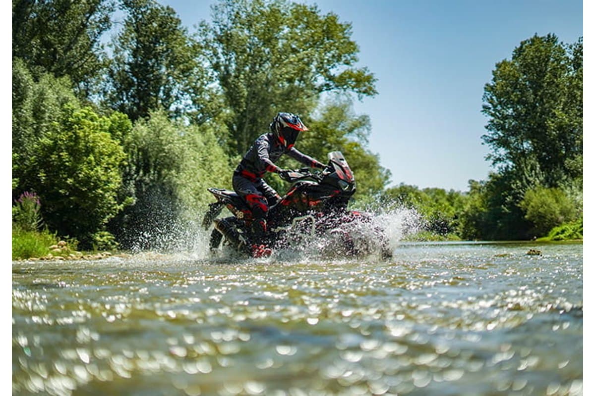Mitas Enduro Trail-XT: a rider crossing a shallow river on an adventure bike, spray across the frame