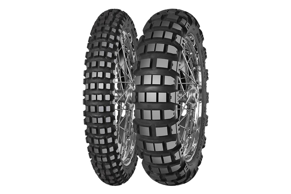 Mitas Enduro Trail-XT+: front and rear pair on chrome spoked rims with a third tire of the same model in the foreground, aggressive square knobs, on white