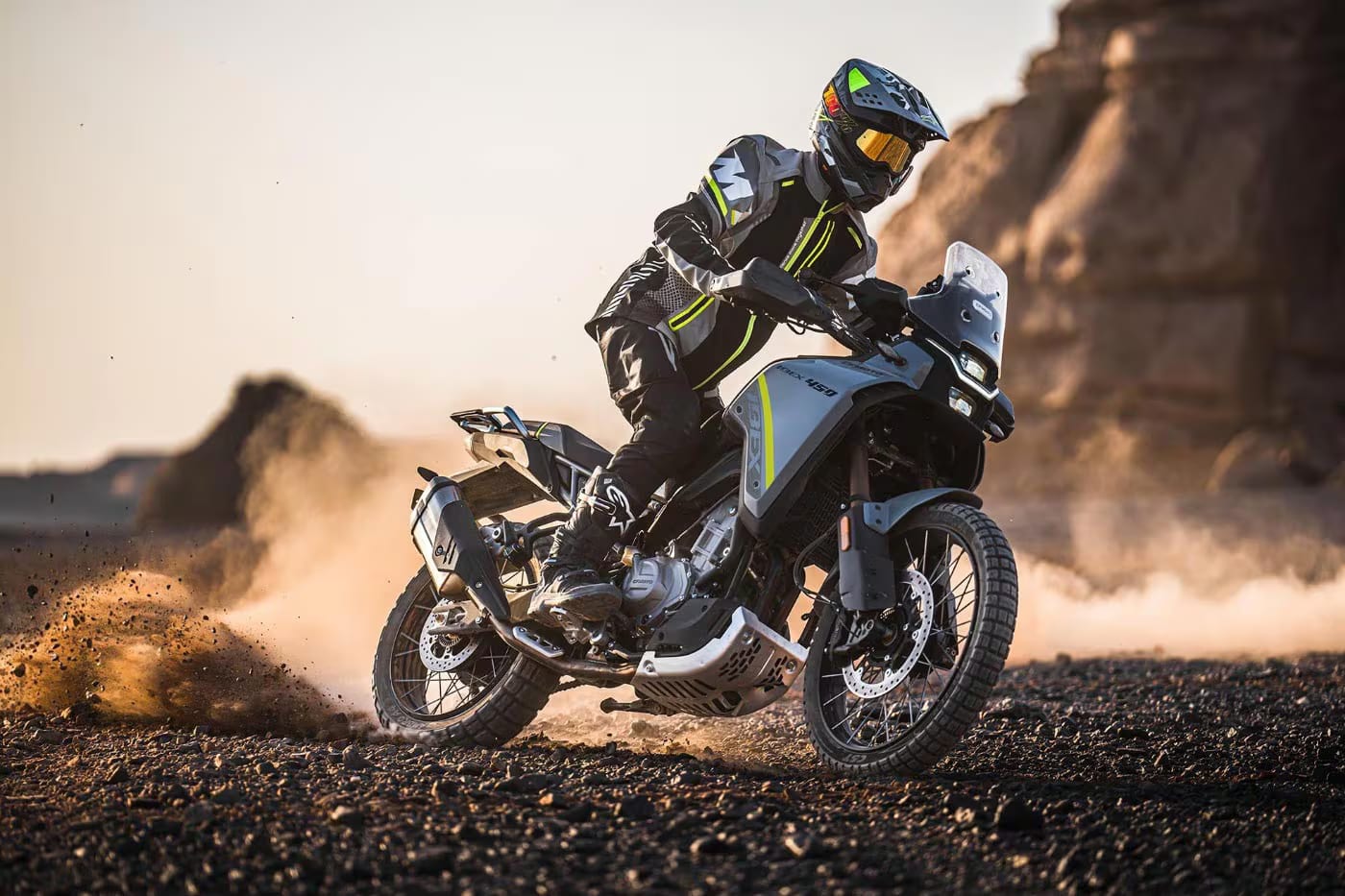 A rider on a CFMoto Ibex 450 adventure bike sliding through desert dirt