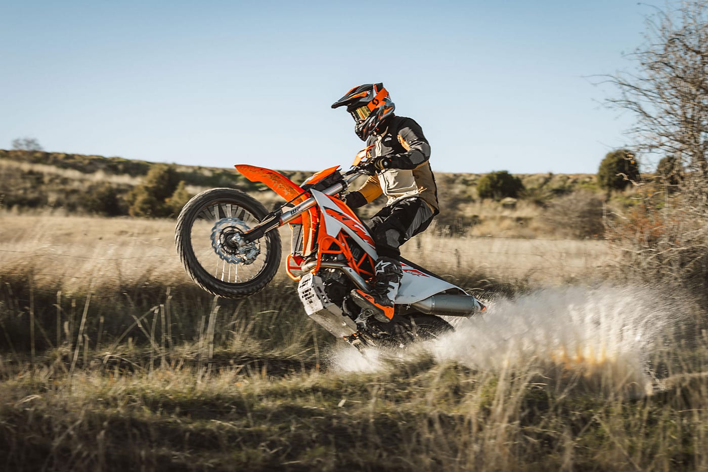 A rider lofting the front wheel of a KTM 690 Enduro R through a grassy field