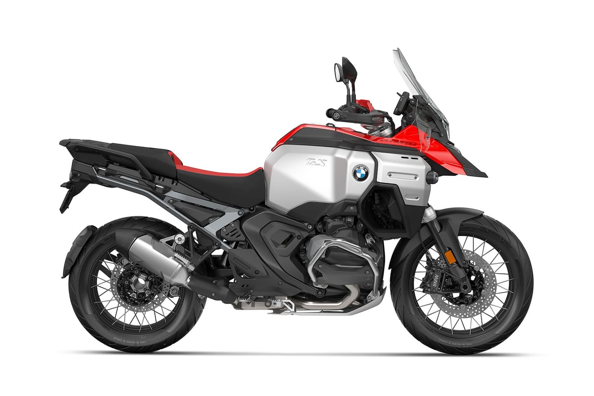 BMW R 1300 GS Adventure in red and silver, left-side studio profile emphasizing the exhaust canister, wire-spoke wheels and luggage rack
