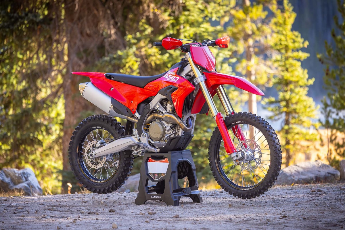2026 Ducati Desmo450 EDX in red and black, left-side studio profile on a wooden stand showing gold forks, spoke wheels and a silver muffler