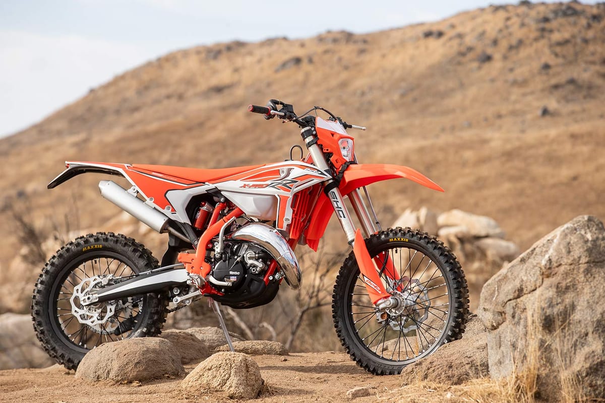 Beta 125 RR X-Pro parked on rocky desert terrain, front three-quarter angle showing the radiator shrouds and knobby Maxxis tires