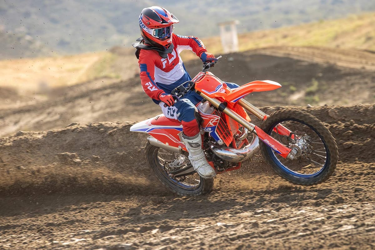 Rider in red and blue gear leaning into a berm on a Beta 125 RR X-Pro two-stroke, roosting dirt on a motocross track