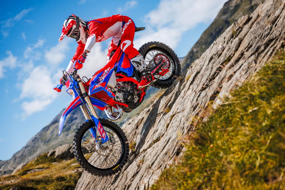 Rider in red gear powering a Beta 300 RR Race up a steep rock face, rear wheel gripping stone as the front end lifts skyward