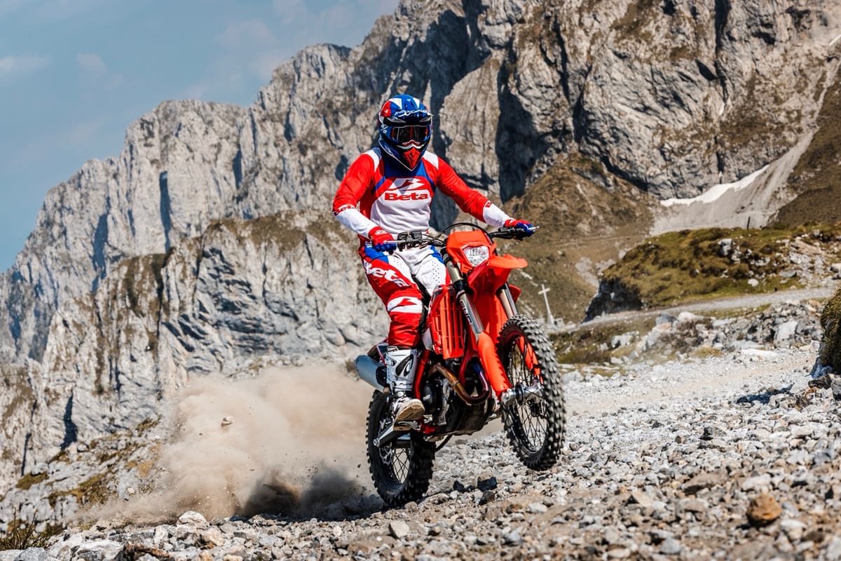 Rider in Beta race gear standing on the pegs of a red Beta 480 RR X-Pro, powering up a loose rocky trail with a plume of dust behind the rear wheel