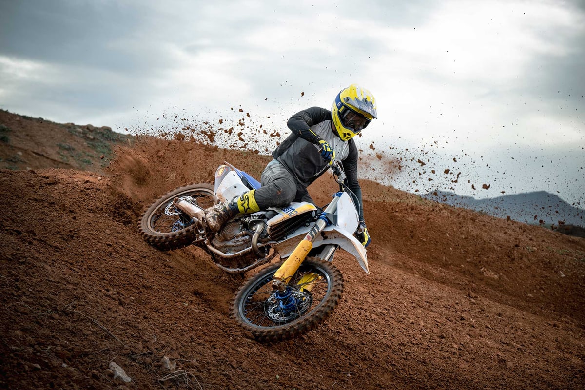 Rider cornering the Husqvarna FC 250 through a rutted red-dirt berm, roost spraying off the rear wheel
