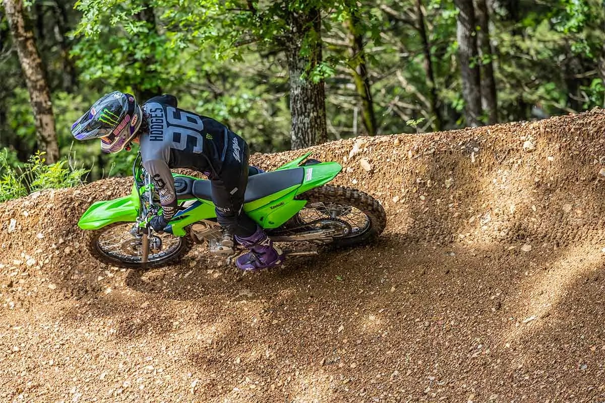 Rider leaning a Kawasaki KLX230R S through a dirt berm, roost spraying from the rear wheel