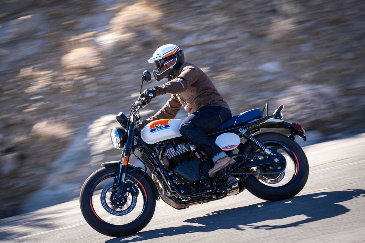 Rider in a white helmet and tan jacket leaning the Bear 650 through a fast road corner in white and blue livery